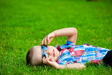 快乐的孩子休息躺在绿草中的太阳镜