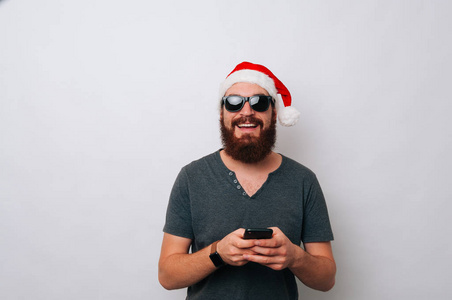 微笑胡子的人与圣诞老人帽子使用电话在白色背景