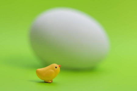 小玩具黄色小鸡附近的大白鸡蛋在绿色背景