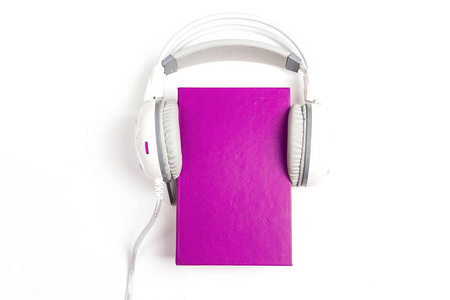 紫色的书, 白色的耳机在白色背景上。有声书的概念。带文本空间的顶部视图