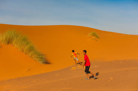 男孩在沙漠中的沙滩上奔跑, 在梅尔祖卡地区。摩洛哥