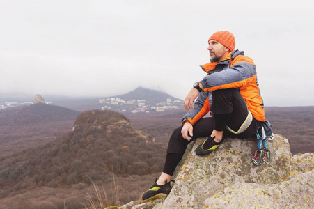 一个登山者在羽绒服和针织帽坐在岩石的顶端休息