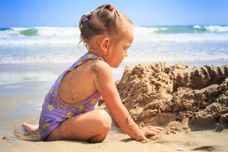 女孩在沙子城堡附近演奏在海滩