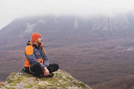 一个登山者在羽绒服和针织帽坐在岩石的顶端休息