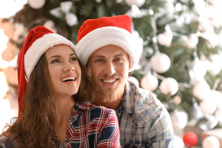 可爱的年轻夫妇在圣诞老人的帽子庆祝圣诞节在家里