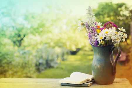 五颜六色的新鲜野生花卉花束在木桌户外与书籍的乡村壶