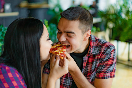 迷恋夫妇吃一块热比萨沿从两侧在比萨店。特写