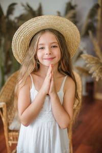 一个可爱的小女孩, 长着金色的头发, 在白色的 sarafan 和一顶草帽在藤椅和芦苇装饰