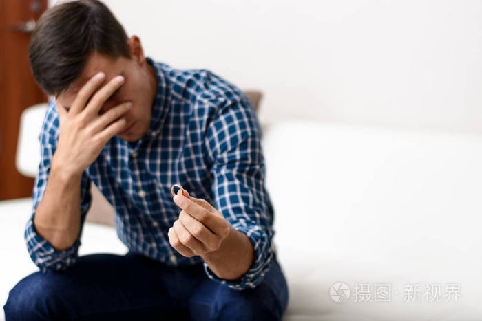 离婚的概念伤心孤独的男子手持订婚戒指坐在家里离婚后的抑郁症选择性
