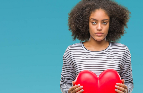 年轻的美国黑人妇女抱着红色的心, 在孤立的背景下, 对聪明的脸上充满自信的表情认真思考