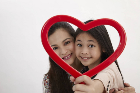 马来母亲和女儿抱着一个红色的心形相框面对摄像头