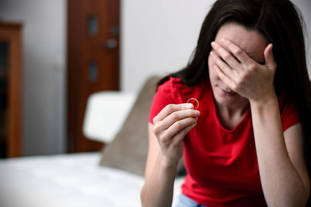 少妇寂寞性照离婚的概念.伤心寂寞的女子手持订婚戒指坐在室内的特写.