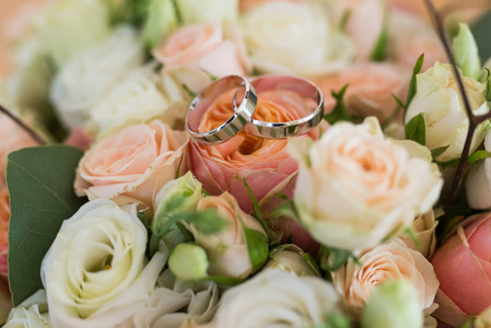 两个婚礼金戒指躺在婚礼花束与橙色和米色玫瑰。婚礼详情