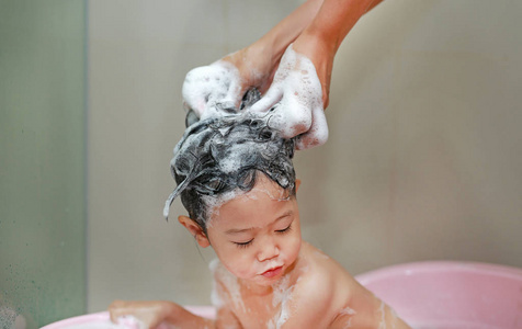 妈妈的手从淋浴里倒水洗小女孩的头发照片