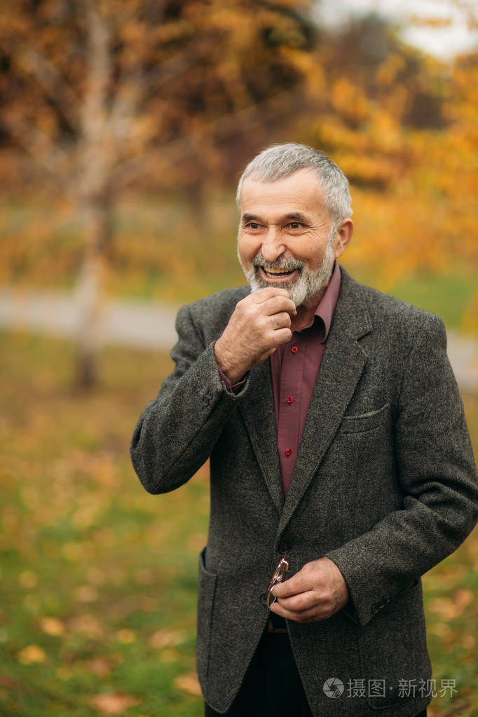 一个戴眼镜的英俊老人正在用手机.秋天在公园漫步