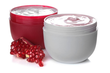 奶油在白色和红色罐子旁边新鲜的石榴在白色隔绝的背景上