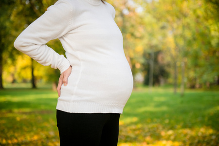 长长的金色卷发抱着她的肚子,看着相机中夏公园可爱微笑年轻孕妇的