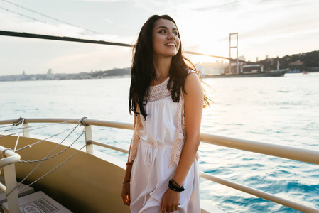 年轻女孩旅行放松而游弋在游艇上看日落，现代著名的大桥上背景