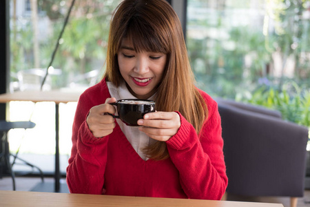 女人在餐馆穿红毛衣。女孩拿着拿铁咖啡杯子