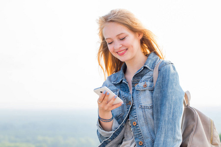 快乐的年轻女人阅读信息, 通过智能手机在互联网上看东西, 在大自然中