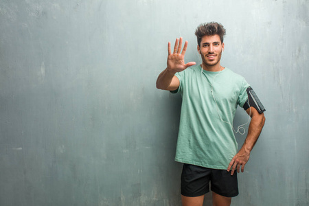 年轻健身男子对一堵墙显示五号, 戴着臂章与电话