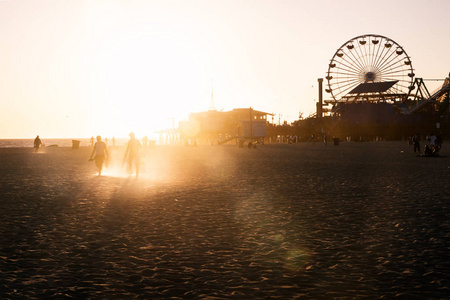 在加利福尼亚州洛杉矶日落时, 沿圣莫尼卡海滩和游乐园漫步的人们的剪影