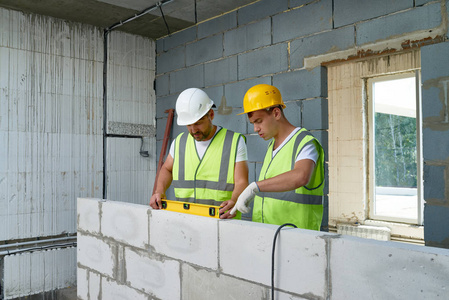 两个建筑工人的肖像穿 hardhats 和反光背心检查混凝土砌块墙体使用水平