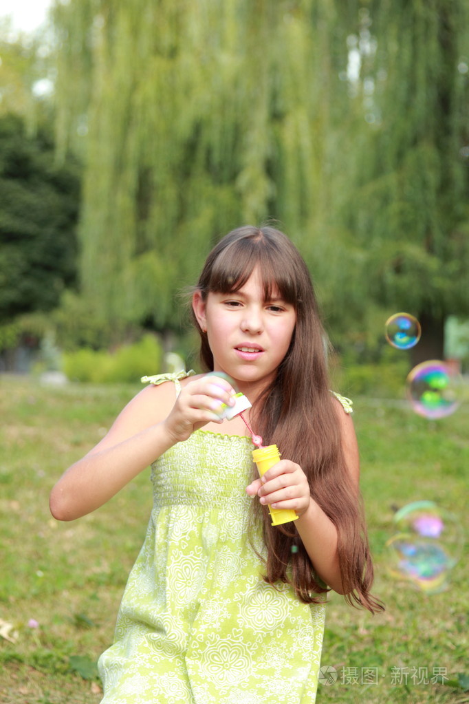 可爱快乐的小女孩坐在草地上，吹肥皂泡