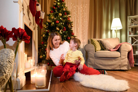 母亲和儿子互相微笑, 圣诞树在他们身后闪闪发亮。圣诞室内设计, 圣诞树装饰圣诞树