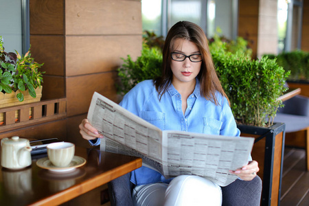 坐在餐厅扶手椅和阅读 newspape 的漂亮女孩