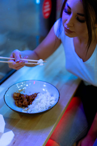 在咖啡馆里用筷子吃亚洲食物的年轻美女特写