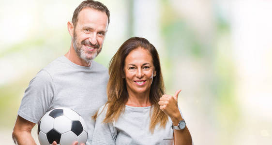 中年拉美裔夫妇持有足球足球在孤立的背景指向和显示与拇指面带微笑的笑脸