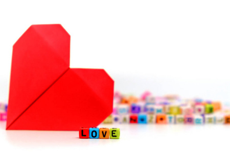 词爱在模糊的红色纸心脏与字母表字母珠背景为爱和情人节概念