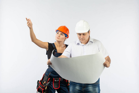 承包商的人讨论建立在白色背景的计划。工头与建设者妇女佩带头盔