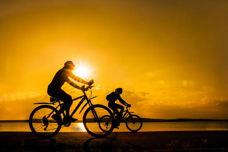运动的朋友在自行车在日落。在海岸骑自行车的剪影。体育在自然背景