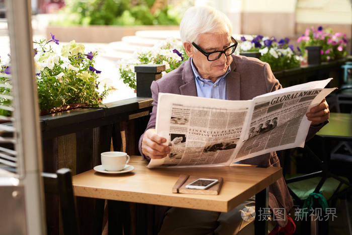 戴眼镜的老人在户外咖啡馆看晨报的肖像