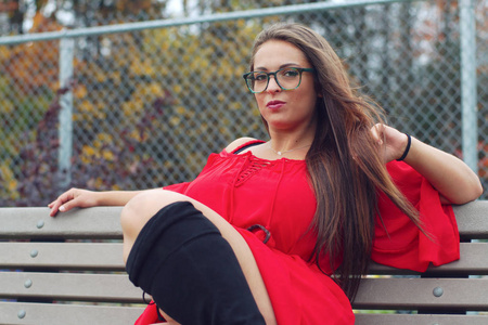 年轻女子红色礼服靴子坐在长凳公园眼镜