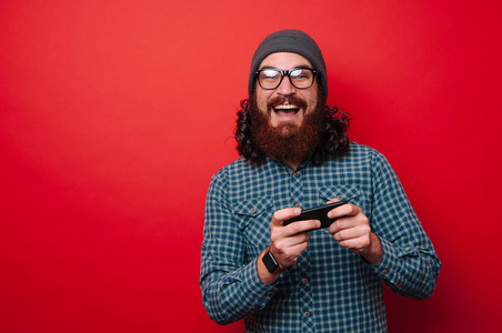 微笑的人与胡子的肖像看着相机和手持手机智能手机在红色背景下