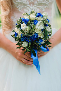 婚礼美丽花束与白色玫瑰和蓝色鲜花在新娘手中的戒指