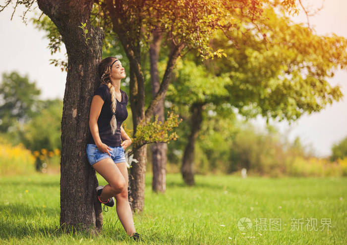 悠闲的女孩在夏日的草地上站在树下