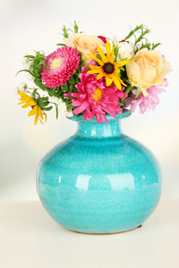 束美丽的鲜艳的花朵在彩色花瓶，木桌上，在明亮的背景上