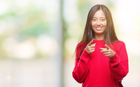 年轻的亚洲妇女穿着冬季毛衣在孤立的背景下, 手指到相机与快乐和滑稽的脸。良好的能量和共鸣