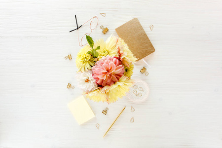 平躺妇女办公室办公桌。女性工作区与粉红色和黄色的大丽花和玫瑰花花束, 配件, 金色的日记, 在白色的木制眼镜