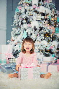积极开朗的女婴坐在圣诞节礼物圣诞树附近。新年快乐