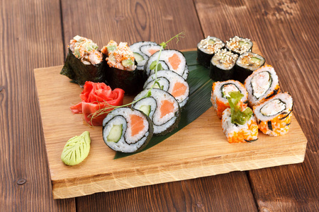 一种有不同类型的寿司的木制盘子。用姜和芥末在木盘子上做寿司和卷