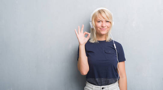 成年白种女人在垃圾灰墙戴耳机做 ok 符号与手指, 优秀的符号