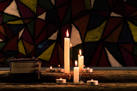 圣经和蜡烛在老橡木桌上。美丽的彩色玻璃窗背景。宗教概念