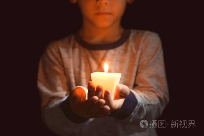 小男孩在黑暗中手持燃烧的蜡烛