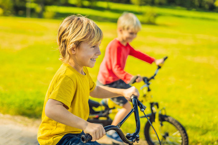 阳光明媚的一天, 两个快乐的男孩在绿色公园骑车