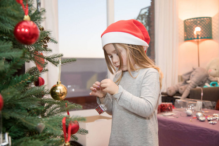 四年金发逗人喜爱的女孩与红色圣诞老人帽子, 装饰圣诞树在家里